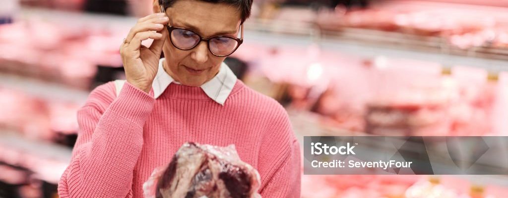 Waist up portrait of adult woman choosing fresh meat shopping for groceries in supermarket, copy space