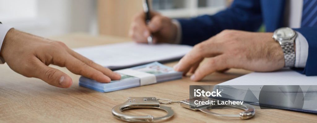 Man hands over cash money to a bondsman asking to release his friend on bail. Unrecognizable businessman gives a bribe to a government official. Crop shot. Handcuffs on a wooden office table close up