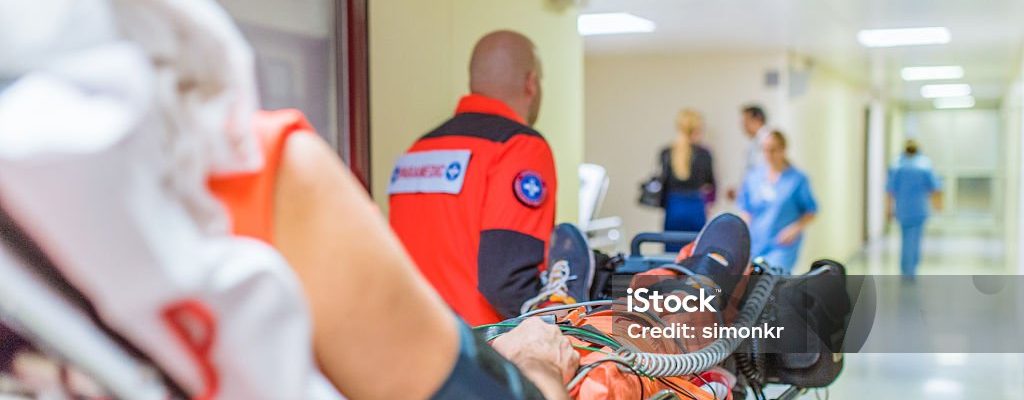 Paramedics wheeling patient on stretcher in hospital's corridor.