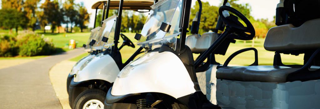 Shot of three golf carts standing side by side next to a golf course